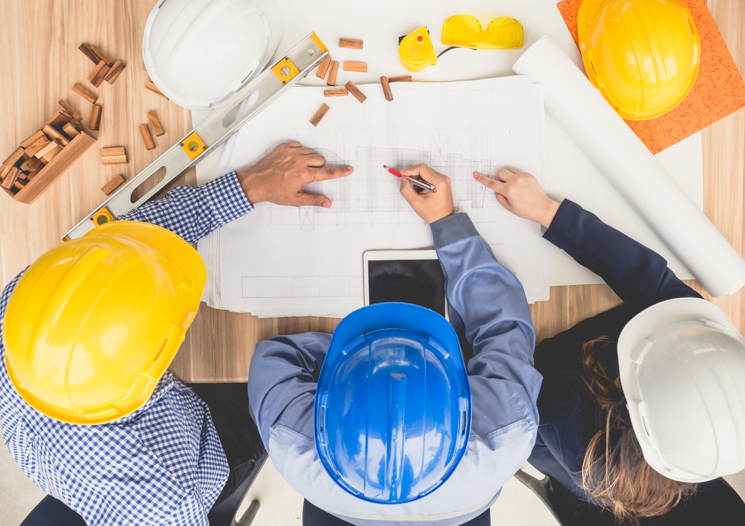 group of engineers and architects discussing on table with drawing/blueprint, wearing safety helmet working for industrial construction and engineering